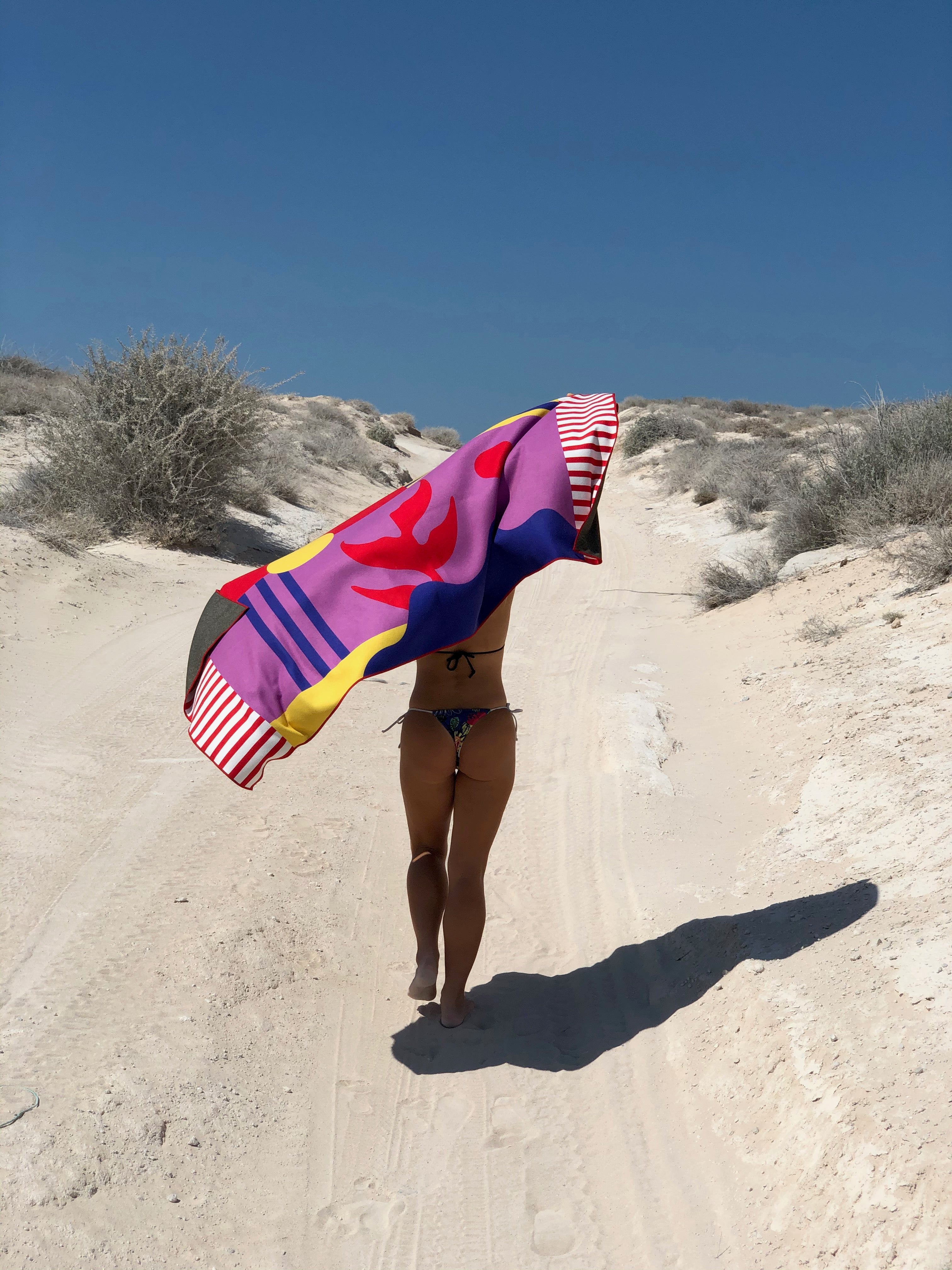 fit young woman walking in the desert holding a purple red vibrant beach towel